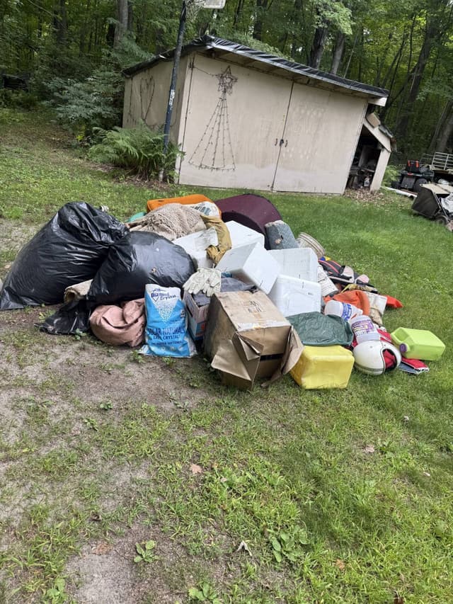 Bagged trash, old carpet and coolers staged for pickup outside a shed